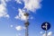 The high mast or pole with spotlights and a traffic sign `go straight or left turn` against a blue sky with white clouds, low a