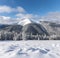 A high mountain with a snow white peak. Landscape on a winter day. Forest. The lawn is covered with snow. Evergreen trees in