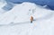 High mountaineer dressed bright orange softshell jacket using a trekking poles ascending the snowy mountain summit. Active people