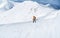 High mountaineer dressed bright orange softshell jacket using a trekking poles ascending the snowy mountain summit. Active people