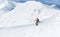 High mountaineer dressed bright orange softshell jacket using a trekking poles descending the snowy mountain summit. Active