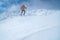 High mountaineer dressed bright orange softshell jacket using a trekking poles descending the snowy mountain summit. Active