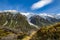 High mountains with snow on top in the winter, beautiful skies and clouds. The grass is yellow in Mount Cook Rd