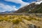 High mountains with snow on top in the winter, beautiful skies and clouds. The grass is yellow in Mount Cook Rd