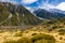 High mountains with snow on top in the winter, beautiful skies and clouds. The grass is yellow in Mount Cook Rd