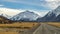 High mountains with snow on top in winter, beautiful sky and clouds. The grass on the road is yellow in Mount Cook Rd