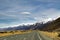 High mountains with snow on top in winter, beautiful sky and clouds. The grass on the road is yellow in Mount Cook Rd