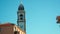 High narrow bell tower with clocks near small country house