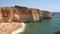 High perspective panning of gold-coloured cliffs, busy beach and turquoise ocean in Benagil beach, Lagoa, Algarve