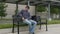 High quality 4k video of a young man who is sitting on a metal bench outside of train and bus station and drinking water