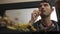 High quality close-up of a young blurred man chatting with friend or family on phone watching tv and having snacks with bottle of