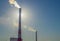 High red and white striped tube lets out white smoke into clear blue sky. Small cloud above pipe on background of electric pole