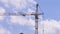 A high-rise construction crane turns against a background of blue sky and clouds.