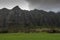 High rocky cliffs border green meadow of Kualoa valley , Oahu, Hawaii, USA