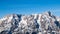 High rocky snowy peak on sunny winter day with blue sky. Alpine mountain ridge