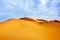 High sand dunes of the Sahara desert against a blue sky with clouds