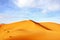 High sand dunes of the Sahara desert against a blue sky with clouds