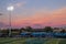 High School football game with night lights on and sun setting in sky