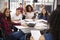 High school kids raise hands, teacher sitting at their desk