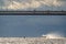 a high-speed passenger hydrofoil boat passes under a cable-stayed bridge in sunny weather, dark storm clouds in the