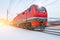 High-speed red locomotive passenger train rides at high speed in winter around the snowy landscape.