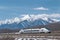 high-speed train zooming past mountain range, with snowcapped peaks in the background