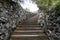 A high staircase with wooden steps extending upward surrounded by stone walls in summer. Travel and mystical places