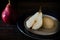 High view of a halved, unpeeled red battler pear on a plate and other pears on the table. Dark background. Organic and natural