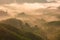 High views with views of mountains and fog interspersed among lush green forests at sunrise, golden light, sky and colorful clouds