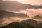 High views with views of mountains and fog interspersed among lush green forests at sunrise, golden light, sky and colorful clouds