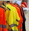 High visibility jackets on a hanger with protective helmets behind, in a work clothes store