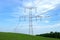 High voltage eletrical towers and lines with blue sky and green meadow. Eletricity towers on a green field. Transmission lines