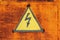 High voltage lightning sign in yellow triangle on rusty metal door, grunge abstract background