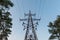 High voltage lines and power pylons. Blue Sky and Forest tree nearby.