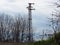 High voltage power lines against gloomy blue sky and leafless trees. Old system electric power grid view. Electric pillars poles.