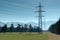 High voltage power lines and tall lattice crosses in rural countryside with snow-capped mountain peaks in the background