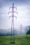 High voltage towers in a middle of forests and meadow. Electricity pylon with dark atmosphere in a nature. Rainy day. Power transm