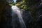 A high waterfall with white splashes of water descends from the mountain and sparkles in the sun.