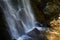 A high waterfall with white splashes of water descends from the mountain and sparkles in the sun.