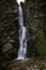 A high waterfall with white splashes of water descends from the mountain and sparkles in the sun.