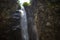 A high waterfall with white splashes of water descends from the mountain and sparkles in the sun.