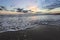 High waves with foam spread on the sand on the coast. Pre dawn time. The light of unbelievable sunset is reflecting on the sea.