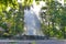 High white fountain against trees in the park with falling shadows on it