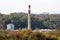 High wide concrete red and white rectangle industrial chimney rising high above industrial complex with new storage tanks