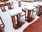 High wooden tables and bar stools of an outdoor cafe stand in a row in winter covered with snow