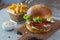 Highigh burger with french fries in small fry basket on concrete surface. Traditional American fastfood.