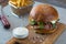 Highigh burger with french fries in small fry basket on concrete surface. Traditional American fastfood.