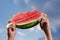 Highly raised children`s hands holding a piece of ripe watermelon against the blue sky