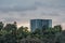 Highrise building peaking over vegetation at sunset with clouds