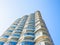 Highrise residential building with curved glazed balconies set against a blue sky. Bottom view